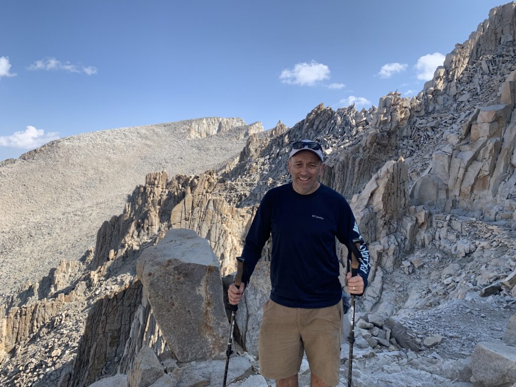 Photo of Brandon, author of Unity and Beyond, hiking a rocky mountain trail, embodying the perseverance behind his conflict resolution steps framework.
