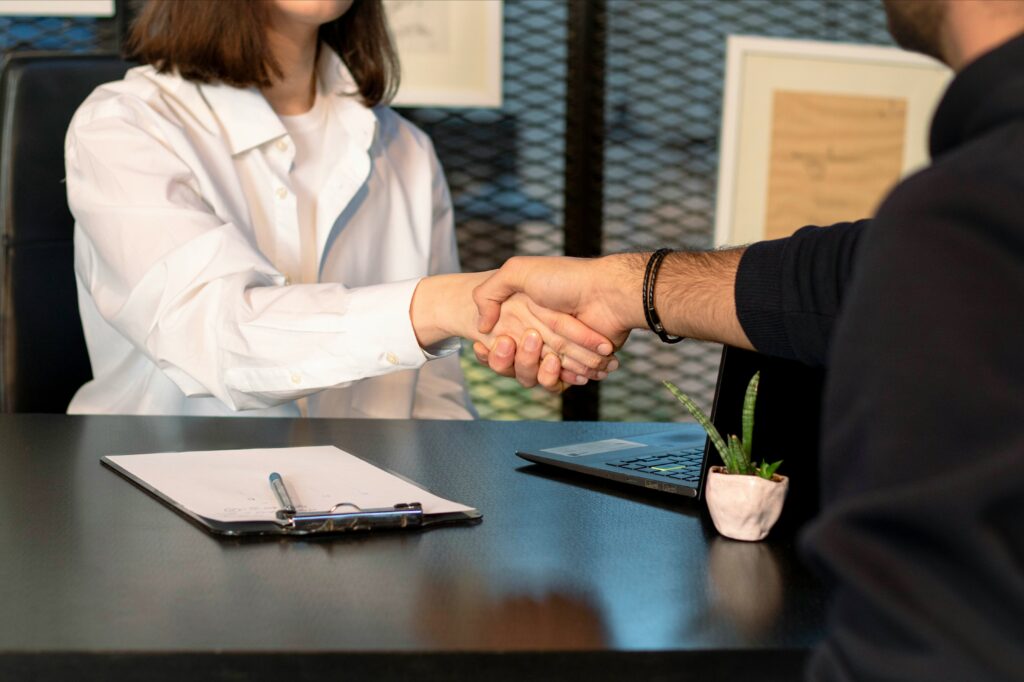Two business professionals shaking hands after closing a deal, representing the shorter sales cycles and client trust built through a book as a business tool.