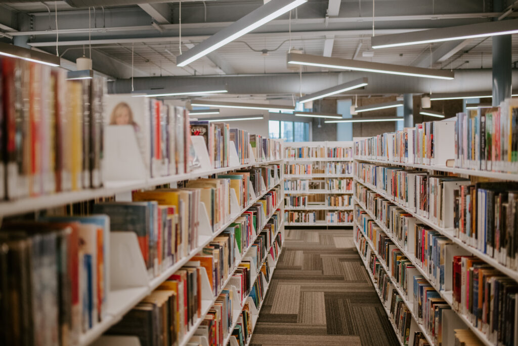 Long aisle of colorful books on white library shelves, representing the ongoing visibility that book promotion services provide for authors after publishing.