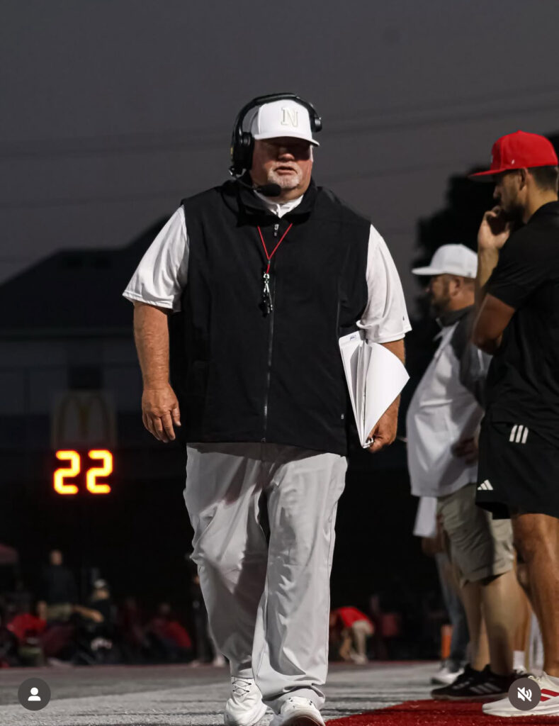 hoto of John Perry, head football coach at Nixa High School, walking the sideline during a night game, personal growth book author.