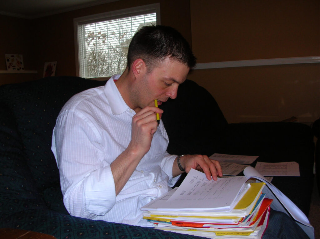 Photo of David Hockman seated on a couch reviewing a thick binder of documents with a pencil, author of religious shame memoir Surgeon Unmasked.