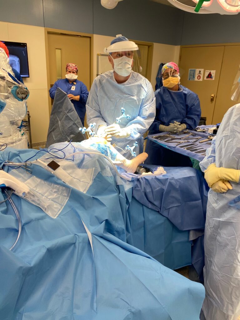 Photo of David Hockman in surgical mask and gown performing an operation, religious shame memoir author and hip and knee surgeon.