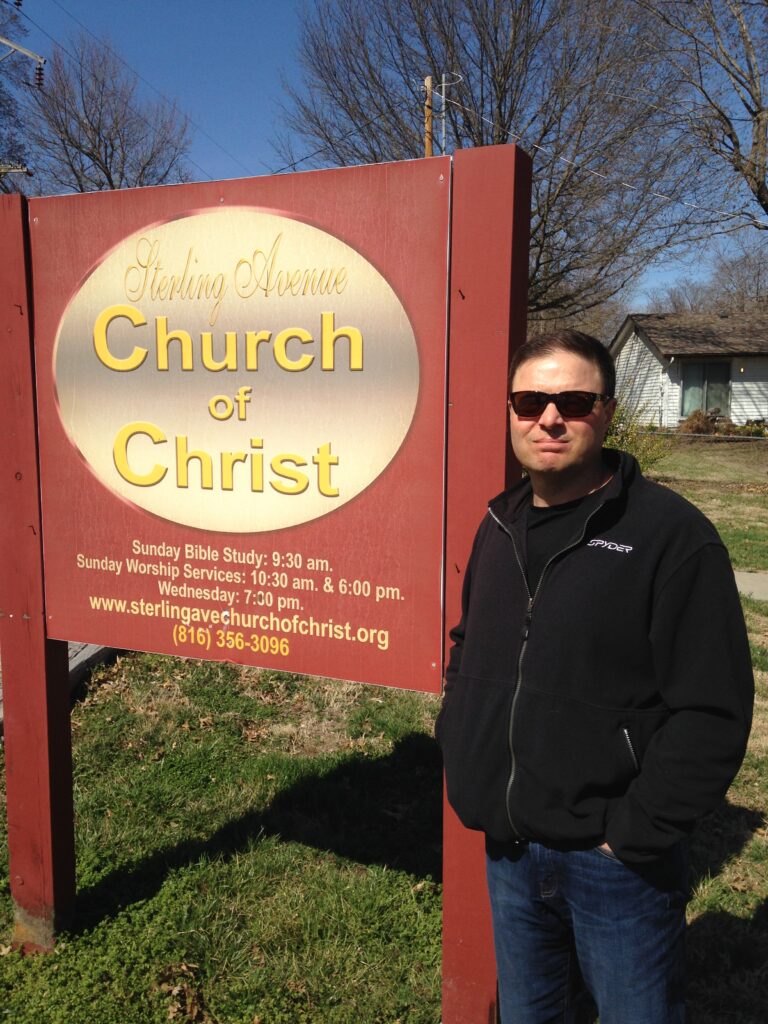 Photo of David Hockman in sunglasses and black jacket standing beside a Sterling Avenue Church of Christ sign, author writing about overcoming religious shame.