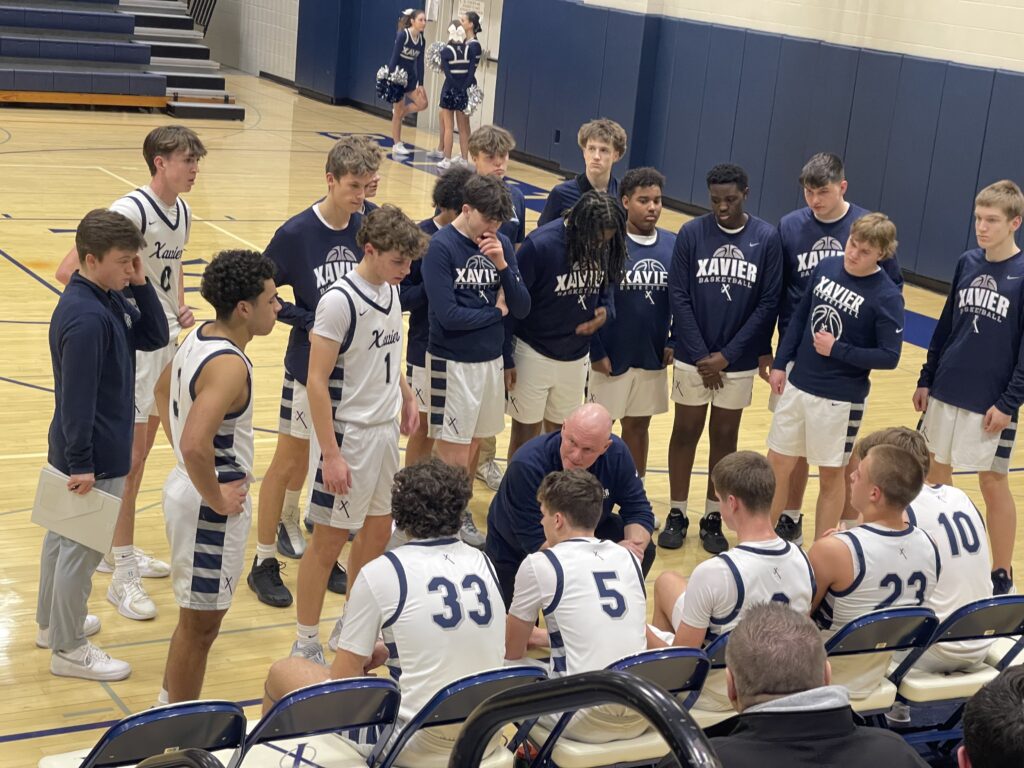 Photo of Wes Bruns huddling with the Xavier basketball team during a timeout.