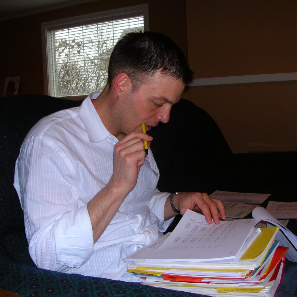 Photo of David Hockman seated on a couch reviewing a thick binder of documents with a pencil, author of religious shame memoir Surgeon Unmasked.