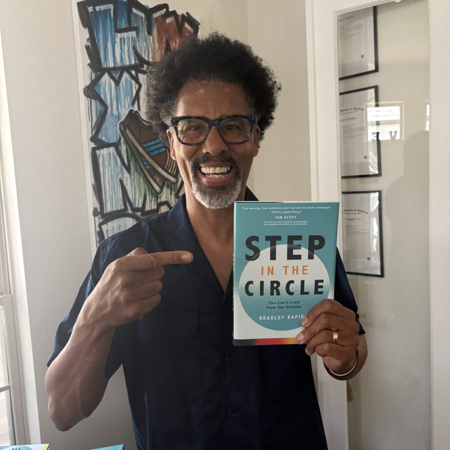 Photo of Bradley Rapier smiling, pointing at his freestyle leadership book, Step in the Circle